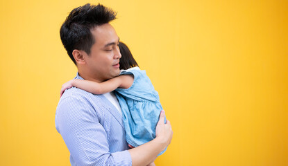 young handsome Asian father holding his daughter in his arms and smiling, isolated on Yellow background.Happy father and daughter.