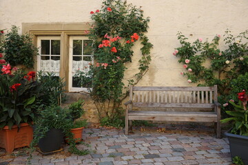 Fototapeta na wymiar Bench with flower pots and closed decorated window in old house in europe, window with glasses and red flowers