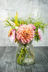 Beautiful bouquet of summer flowers in a green glass vase. Black table, gray background. Dahlias, celosia, cosmos, and aster flowers.