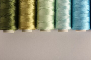 Different colorful sewing threads on light grey background, flat lay. Space for text