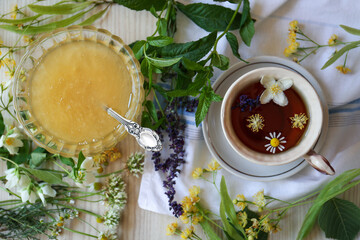 Cup of hot aromatic tea, honey and different fresh herbs on white wooden table, flat lay