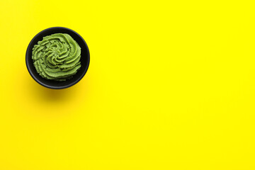 Bowl with swirl of wasabi paste on yellow background, top view. Space for text