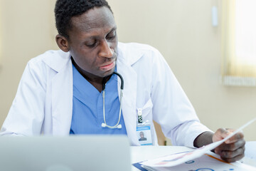 African American man doctor using laptop and paperwork checking report at table office.