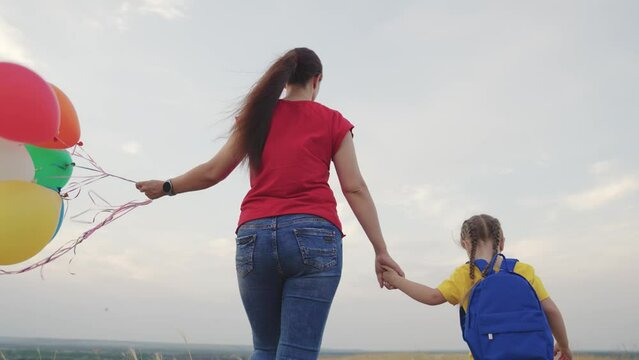 mother holds little child daughter with backpack against sky. happy family life. mom with kid girl walks along rural road park. teamwork. family adventures. travel naturechild hand parent
