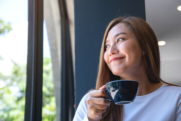 Portrait image of a young woman holding and drinking hot coffee in cafe