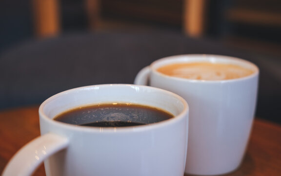 Closeup image of two white cups of hot coffee on wooden table in cafe