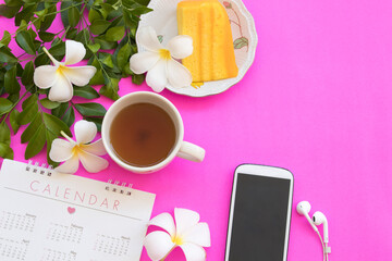 hot tea, orange cake dessert snack, calendar, mobile and flowers frangipani arrangement flat lay...