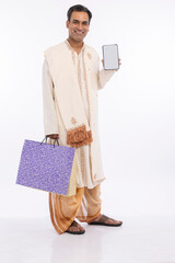 Bengali man holding shopping bags and showing mobile phone screen on occasion of durga puja festival
