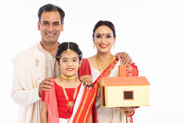Happy bengali parents with girl holding model house in traditional clothing
