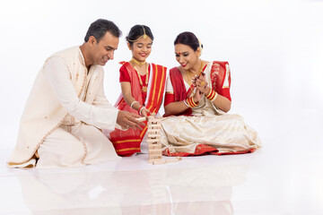 Happy bengali parents with daughter playing jenga together in traditional clothing
