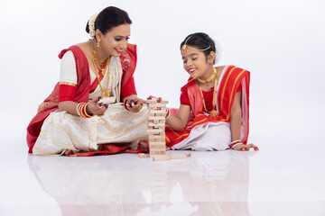 Happy bengali mother with daughter playing jenga together in traditional clothing
