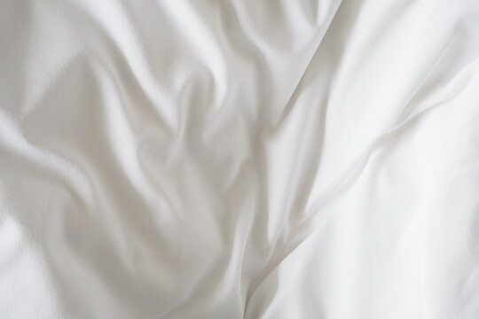 Closeup of beautiful white shiny crumpled polyester fabric sheets on the bed with warm motion and feeling for background and decoration Cloth washing and laundry concept at home