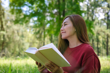 Obraz premium Portrait of a beautiful young asian woman reading a book while sitting in the park