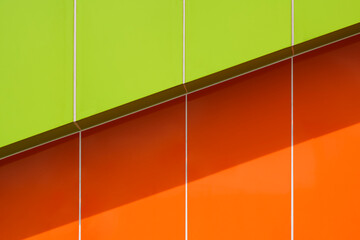Sunlight and shadow on surface of vibrant green and orange aluminum composite tiles wall outside of modern building