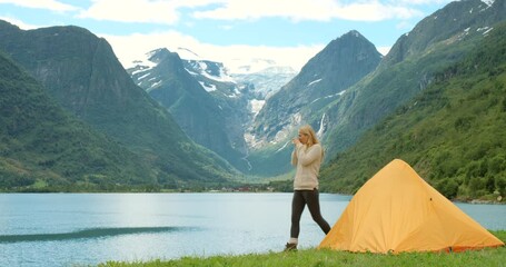 Camping, travel and nature trip of a female waking up to a beautiful winter morning in nature. Back view of a young woman drinking camp coffee outside by mountains with snow, green grass and water