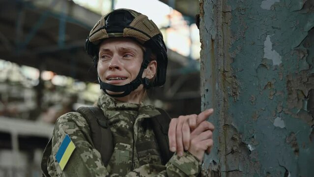 Ukrainian female soldier crying emotionally while standing alone among destroyed steel plant. Desperation during war. Aggression and terrorism in Ukraine.