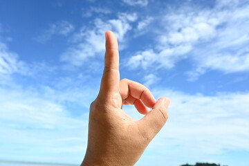Woman pointing at something on blue sky background, closeup of hand and index finger