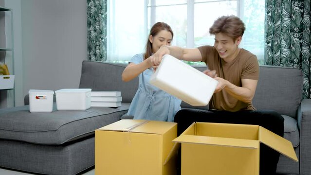Asian young cute couple packing their stuff together in old house on moving day. Happy wife and husband close boxes parcels and prepare to move to a new home, Relationship and relocation concept.