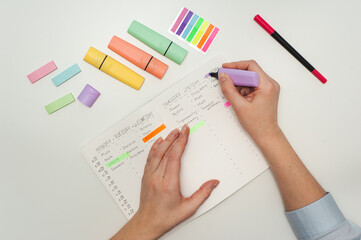 Planning the school year. Drawing up a student schedule. The girl makes edits with a purple marker in the planner on the white table. Multicolored markers and stickers on a white table.