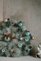 Traditional Christmas decorative wreath over grey marble wall. Round fir garland with snow, blue glitter balls and pine cones. Copy space for New Year congratulations. Holiday interior details.