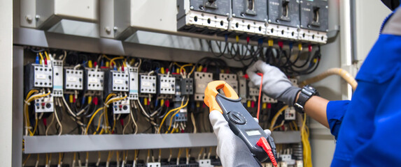 Electricity and electrical maintenance service, Engineer hand holding AC voltmeter checking electric current voltage at circuit breaker terminal and cable wiring main power distribution board.