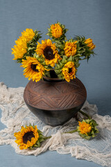 A bunch of yellow sunflowers in a clay pot on a blue background and a brown table. Fabric drapery. Ommage van Gogh