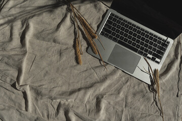 Aesthetic luxury bohemian minimalist home office workspace desk. Laptop computer, dried grass with warm sunlight shadows on linen fabric. Flat lay, top view work, business concept