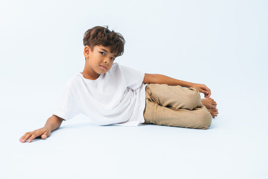 Lying on the floor on his side Indian boy against bluish white background