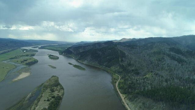 From great height majestic winding serpentine river flows into Lake Baikal. Incredible epic natural landscape Russia Siberia. Stream among mountains. Country road next to coast. Dramatic clouds. Stock