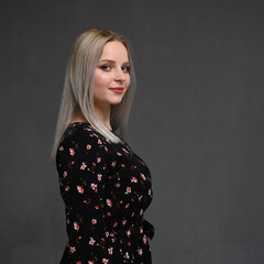 Side view portrait of a beautiful young blonde woman with long straight hair on a gray background. Looking camera