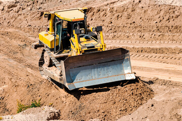A powerful bulldozer in a sand pit is planning a site. Extraction of sand in an open pit. natural building materials.