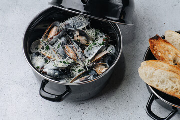 Cooked oysters in a pot sprinkled with parmesan and greens. On a table