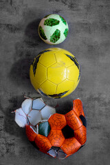 Pyramid of three soccer balls, torn orange big old ball, used yellow, new green small one for mini football. Vertical close up abstract sports pattern, gray background, copy space. Evolution concept.