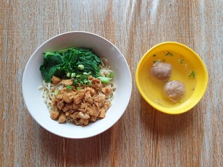 simple chicken noodles with vegetables and chicken topping with chopped spring onions, served in a white bowl, and served with meatballs in a small yellow bowl