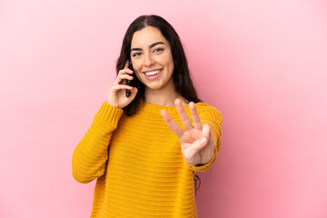 Fototapeta na wymiar Young caucasian woman using mobile phone isolated on pink background happy and counting three with fingers