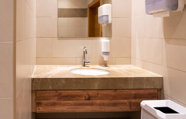 Sink in modern public toilet with paper towels and wastebasket