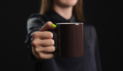 mockup of a brown mug in female hand on a dark background