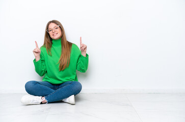 Young caucasian woman sitting on the floor isolated on white background pointing up a great idea