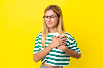 Blonde Uruguayan girl isolated on yellow background having a pain in the heart