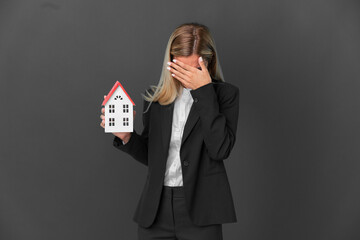 Blonde Uruguayan girl holding a house toy isolated on black background with tired and sick...