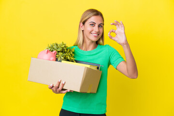 Young Uruguayan girl making a move while picking up a box full of things isolated on yellow...