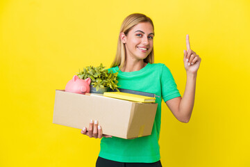 Young Uruguayan girl making a move while picking up a box full of things isolated on yellow background showing and lifting a finger in sign of the best