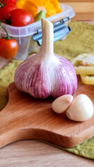 Garlic close-up.Fresh tasty colorful vegetables as yellow pattison, paprika, onion, cherry tomatoes for cooking on brown cutting board laying on green towel.