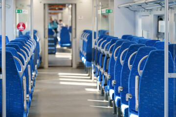 Interior of modern passenger high-speed express train, row of empty blue fabric soft seats selective soft focus. Inside the train carriage with comfortable and colorful chairs. Public transportation
