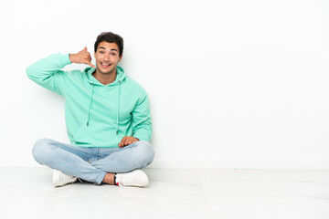 Caucasian handsome man sitting on the floor making phone gesture. Call me back sign