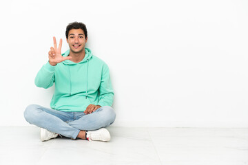 Caucasian handsome man sitting on the floor happy and counting three with fingers