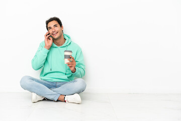 Caucasian handsome man sitting on the floor holding coffee to take away and a mobile