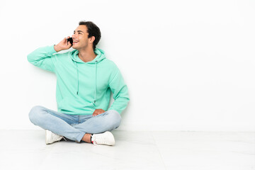 Caucasian handsome man sitting on the floor keeping a conversation with the mobile phone