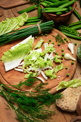 Obraz na płótnie Canvas vegetables on a wooden kitchen board, green onions, dill and peas, sliced cabbage on a wood background, concept of fresh and healthy food, still life
