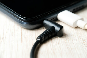 Modern smartphone plugged in power and audio cables on the table. Modern technology concept. Selective focus